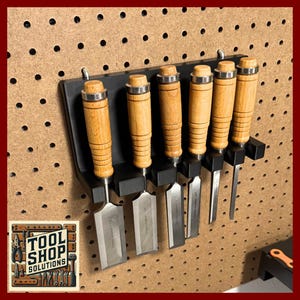 May include: A set of six wood-handled chisels displayed on a black holder, mounted on a pegboard. The chisels have silver blades and are arranged in a row. The logo "TOOL SHOP SOLUTIONS" is visible in the lower left corner.