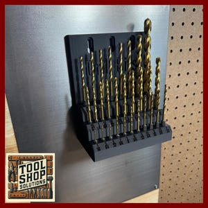 May include: A set of gold-colored drill bits in a black organizer. The drill bits are arranged vertically, with sizes labeled along the bottom. The organizer is mounted on a dark gray metal sheet. The Tool Shop Solutions logo is in the lower left corner.