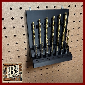 May include: A set of gold-colored drill bits in a black holder, labeled "Metric Drill Bit". The drill bits are arranged by size, with measurements from 1.5 to 4. The holder is mounted on a pegboard.