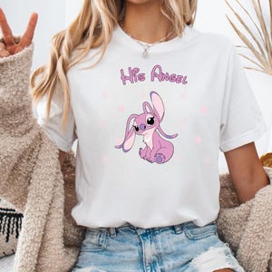 Puede incluir: Camiseta blanca con un personaje Stitch rosa y el texto "His Angel" impreso en ella.