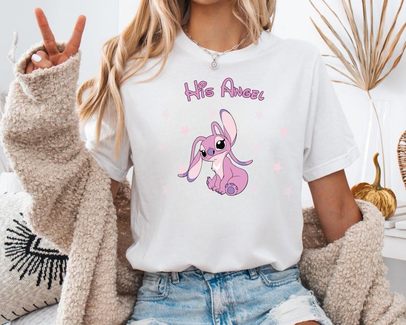 Puede incluir: Camiseta blanca con un personaje Stitch rosa y el texto "His Angel" impreso en ella.