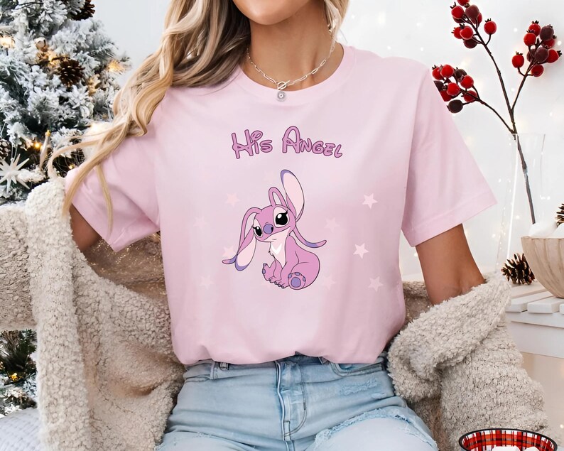 Puede incluir: Camiseta rosa con un personaje de dibujos animados de Stitch y el texto "His Angel" impreso en la parte delantera.