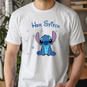 Puede incluir: Camiseta blanca con un personaje de dibujos animados Stitch azul sentado sobre un fondo blanco con estrellas azules. El texto "Her Stitch" est&aacute; impreso en negro sobre el personaje.