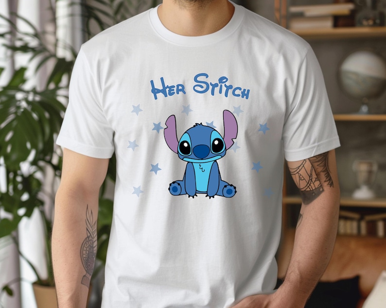 Puede incluir: Camiseta blanca con un personaje de dibujos animados Stitch azul sentado sobre un fondo blanco con estrellas azules. El texto "Her Stitch" est&aacute; impreso en negro sobre el personaje.