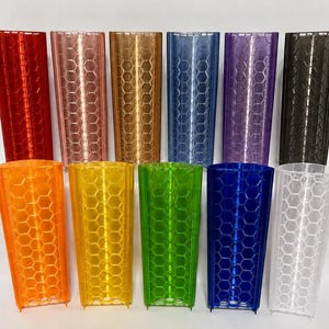 Könnte beinhalten: Eine Sammlung von elf halbtransparenten, zylindrischen Behältern mit einem sich wiederholenden hexagonalen Wabenmuster. Das Set enthält Artikel aus Kunststoff in Rot, Kupfer, Gold, Blau, Lila, Schwarz, Orange, Gelb, Grün, Dunkelblau und Transparent.