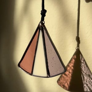 May include: A stained glass suncatcher in the shape of a pyramid with three panels. The panels are pink, white, and purple.