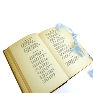 May include: An open book with a blue ribbon bookmark. The book is titled "Poems of Longfellow" and contains the poem "Mad River" by Henry Wadsworth Longfellow. The poem is about a river that flows through a forest and is a symbol of life and death.