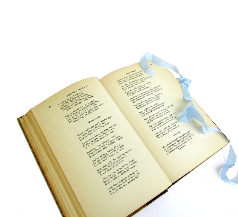 May include: An open book with a blue ribbon bookmark. The book is titled "Poems of Longfellow" and contains the poem "Mad River" by Henry Wadsworth Longfellow. The poem is about a river that flows through a forest and is a symbol of life and death.