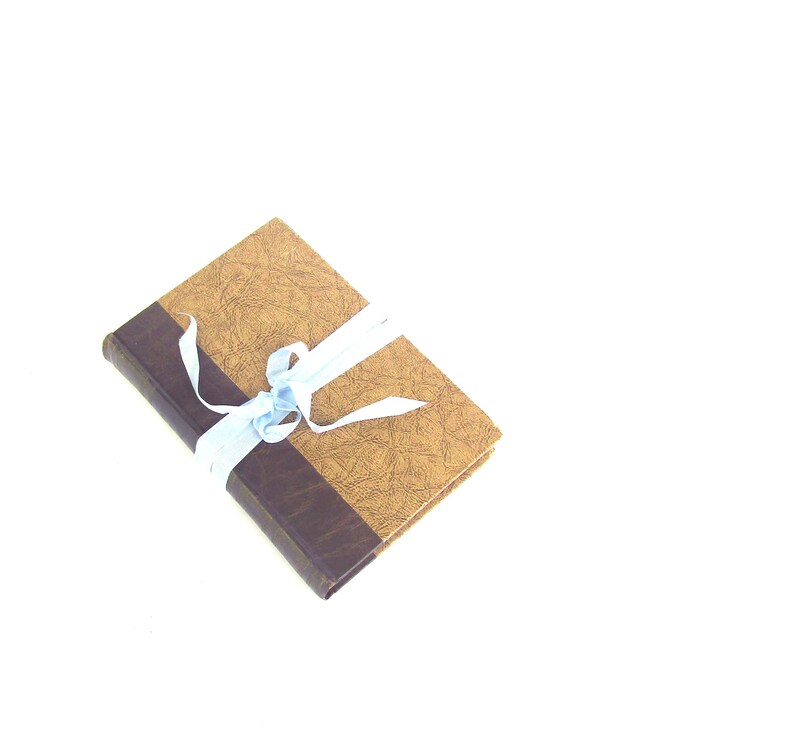 May include: A brown book with a textured cover is tied with a light blue ribbon.