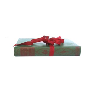 May include: A green hardcover book with a red ribbon tied around it. The book's title is "Alice's Adventures in Wonderland" by Lewis Carroll.