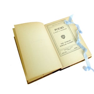 May include: An open book with a light blue ribbon bookmark. The book is titled "Poems" by Henry W. Longfellow. The book is part of "The World's Popular Classics" series.