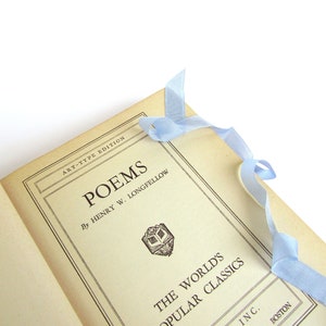 May include: A vintage book titled "Poems" by Henry W. Longfellow. The book is part of "The World's Popular Classics" series and has a light blue ribbon bookmark.