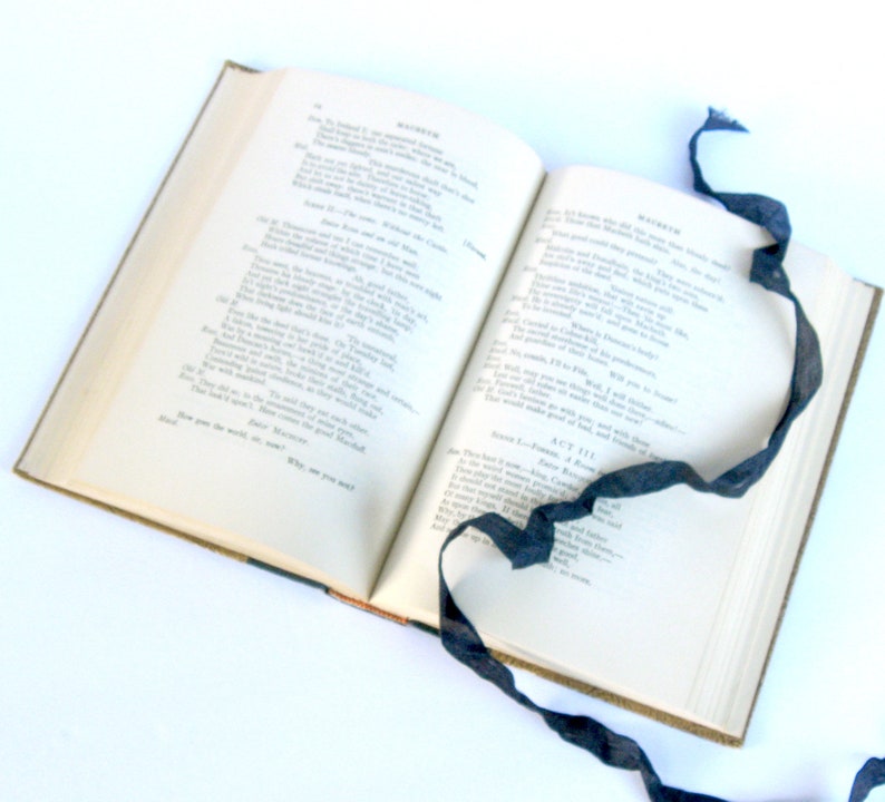 May include: An open book with a black ribbon bookmark. The book is titled "Macbeth" and the pages contain text from Act III, Scene 1.