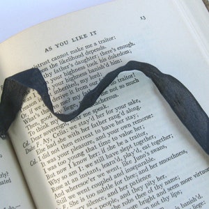 May include: A close-up of a book with a black ribbon bookmark. The book is open to a page with the title "As You Like It" and a passage of text from the play. The text is in black and white.