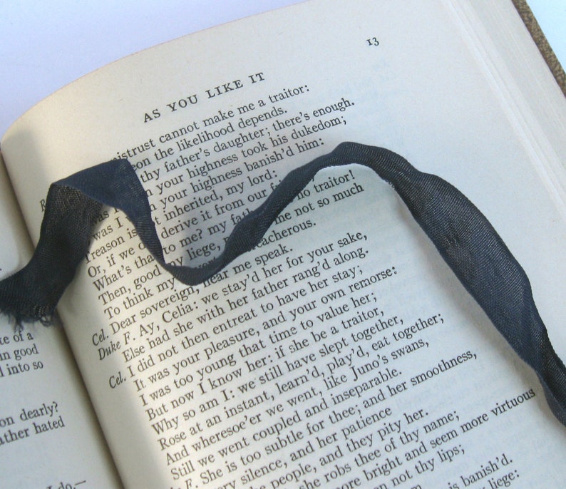 May include: A close-up of a book with a black ribbon bookmark. The book is open to a page with the title "As You Like It" and a passage of text from the play. The text is in black and white.