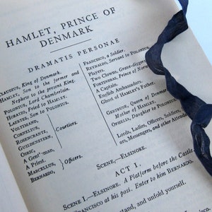 May include: A close-up of a page from a book with the title "Hamlet, Prince of Denmark" and a list of characters from the play. The text is printed in black ink on white paper.