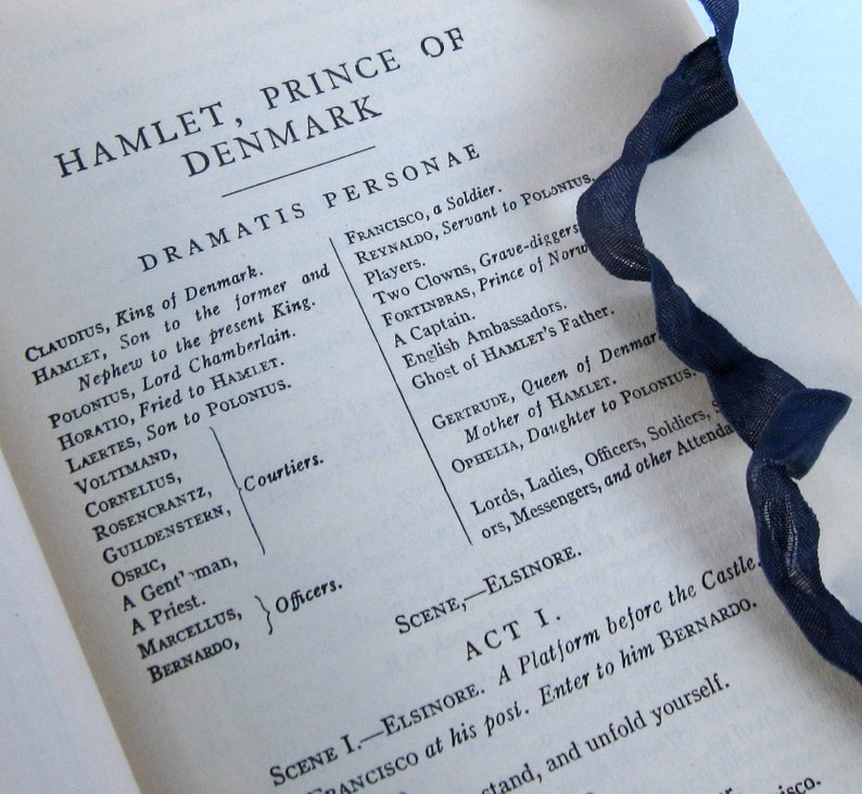 May include: A close-up of a page from a book with the title "Hamlet, Prince of Denmark" and a list of characters from the play. The text is printed in black ink on white paper.