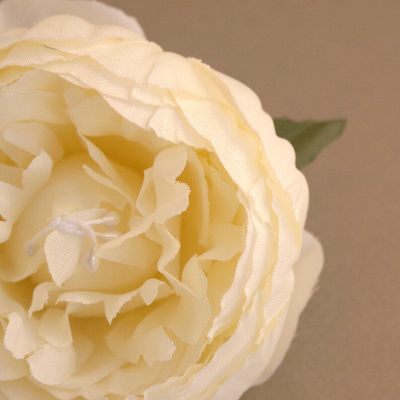 May include: A close-up of a cream-coloured silk flower with a ruffled texture. The flower is in focus, while the background is blurred.