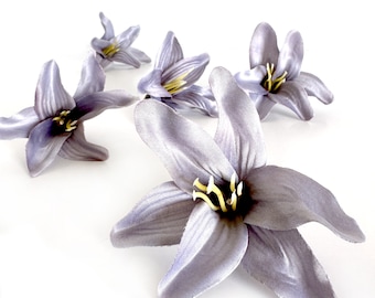 May include: Five artificial lavender lilies with yellow centers. The lilies are arranged on a white background.