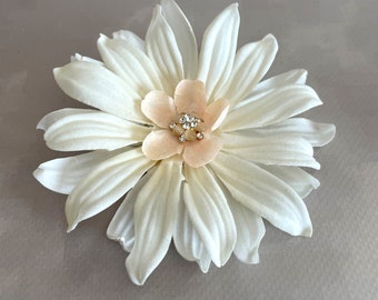 May include: A white fabric flower with a peach-colored center and a rhinestone embellishment.
