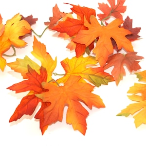 May include: A garland of artificial fall leaves in shades of orange, yellow, and red. The leaves are made of fabric and have a realistic appearance.
