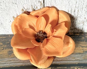 May include: A single, large, peach-colored fabric flower with a brown center. The flower is lying on a rustic wooden surface.