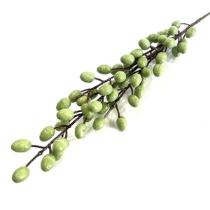 May include: A sprig of artificial green berries with brown stems. The berries are clustered together in a cascading arrangement.