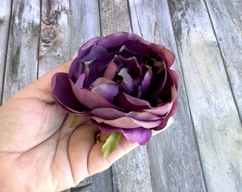 May include: A large, deep purple artificial flower with a ruffled texture. The flower is held in a hand.