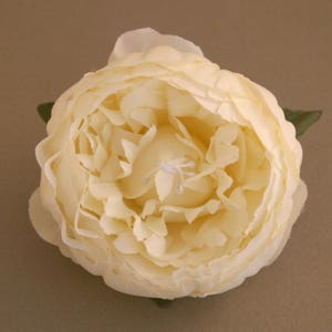 May include: A single, cream-coloured artificial peony flower with a layered, ruffled appearance. The flower is closed, with the petals tightly packed together.