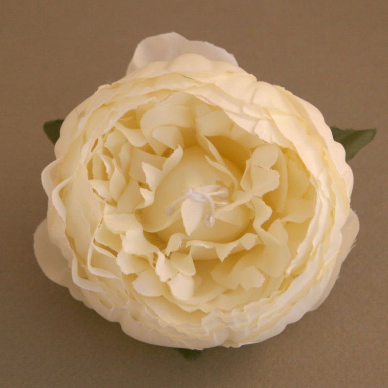 May include: A single, cream-coloured artificial peony flower with a layered, ruffled appearance. The flower is closed, with the petals tightly packed together.
