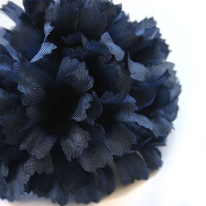 May include: A large, navy blue fabric flower with a ruffled texture. The flower is made of many layers of fabric, creating a full and fluffy appearance.
