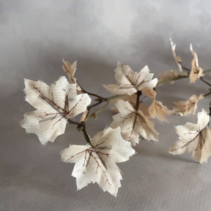 May include: A close-up of a decorative vine with fabric leaves. The leaves are off-white with brown veining, and the stems are a muted green. The leaves are shaped like maple leaves.