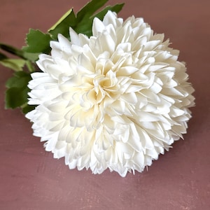 May include: A single white silk flower with a layered, pom-pom style. The flower is made of soft, delicate fabric and has a realistic appearance.