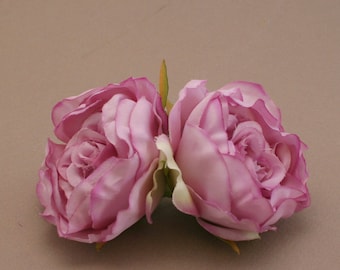 May include: Two pink silk rose flower heads with green stems. The roses are arranged side by side, with the petals overlapping.