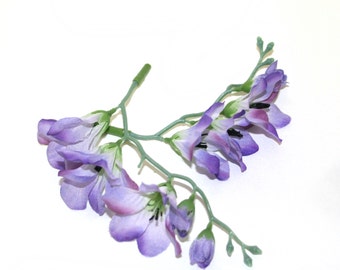 May include: A sprig of artificial purple flowers with green stems and leaves. The flowers are arranged in a cluster and have a delicate, realistic appearance.