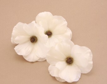 May include: Three white flowers with brown centers. The flowers are arranged in a cluster on a light brown background.