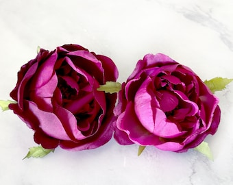 May include: Two magenta silk rose flower heads with green stems and leaves.