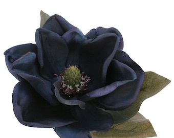 May include: A large, dark blue magnolia flower with a green and purple center and green leaves. The petals have a subtle sheen, and the flower is set against a white background. The flower is a realistic, artificial floral arrangement.