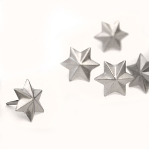 May include: Five silver star-shaped embellishments with a pointed tip on a white background. One star is slightly offset from the others.