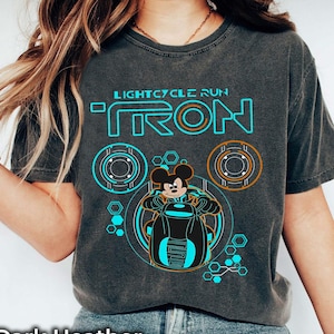 May include: A dark heather grey t-shirt with a graphic of Mickey Mouse riding a lightcycle from the movie Tron. The graphic includes the text "LIGHTCYCLE RUN TRON".