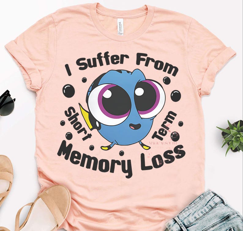 May include: A light pink t-shirt featuring a cartoon image of Dory from Finding Nemo. The blue fish has large eyes and is surrounded by the text "I Suffer From Short Term Memory Loss."