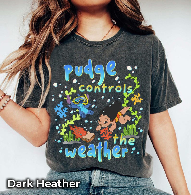 Puede incluir: Camiseta gris oscuro con un gr&aacute;fico colorido que dice "Pudge controls the weather". El dise&ntilde;o incorpora personajes de dibujos animados y motivos acu&aacute;ticos. Esta camiseta es una prenda casual.