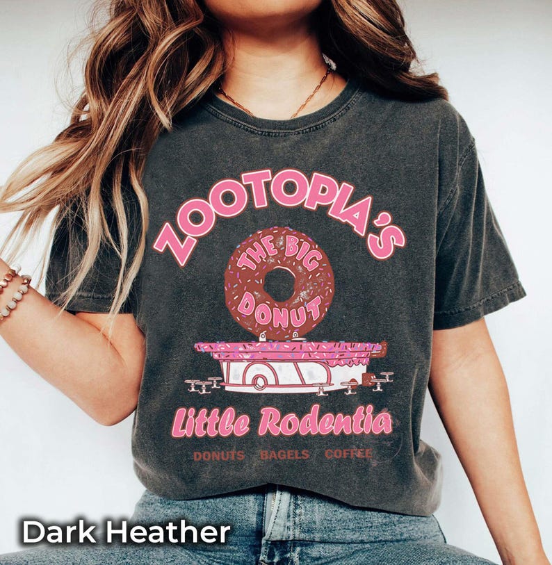 Puede incluir: Camiseta gris oscuro con un gr&aacute;fico rosa. El gr&aacute;fico dice "Zootopia's The Big Donut" encima de un carrito de comida rosa y blanco con "Little Rodentia" y "Donuts Bagels Coffee".