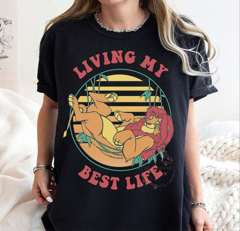 May include: Black t-shirt featuring a cartoon lion lounging in a circle with bamboo accents and the text "LIVING MY BEST LIFE" in red and orange. The lion is orange and yellow.