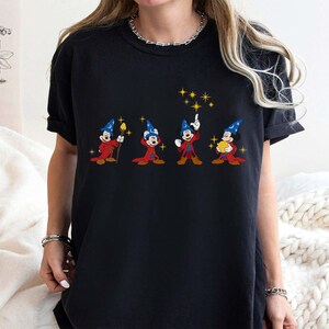 May include: Black t-shirt featuring a graphic of Mickey Mouse in a wizard costume. The design shows Mickey in different poses with a red robe, blue hat, and yellow stars. The shirt is a comfortable, casual style.