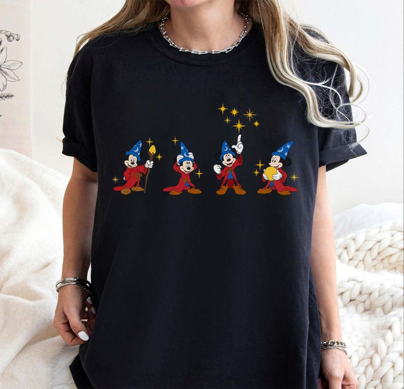 May include: Black t-shirt featuring a graphic of Mickey Mouse in a wizard costume. The design shows Mickey in different poses with a red robe, blue hat, and yellow stars. The shirt is a comfortable, casual style.