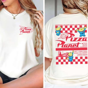 May include: Cream-colored t-shirt with red Pizza Planet logo on the front and back. The back features the text "Interstellar Fast-Food Fueling Station" and cartoon aliens. The shirt also has the text "Pizzas, Salads, Snacks, Beverages".