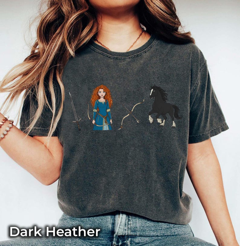 May include: Dark heather gray t-shirt featuring a cartoon illustration of a red-haired woman in a blue dress, a black horse, a sword, and a bow and arrow. The text "Dark Heather" is at the bottom.