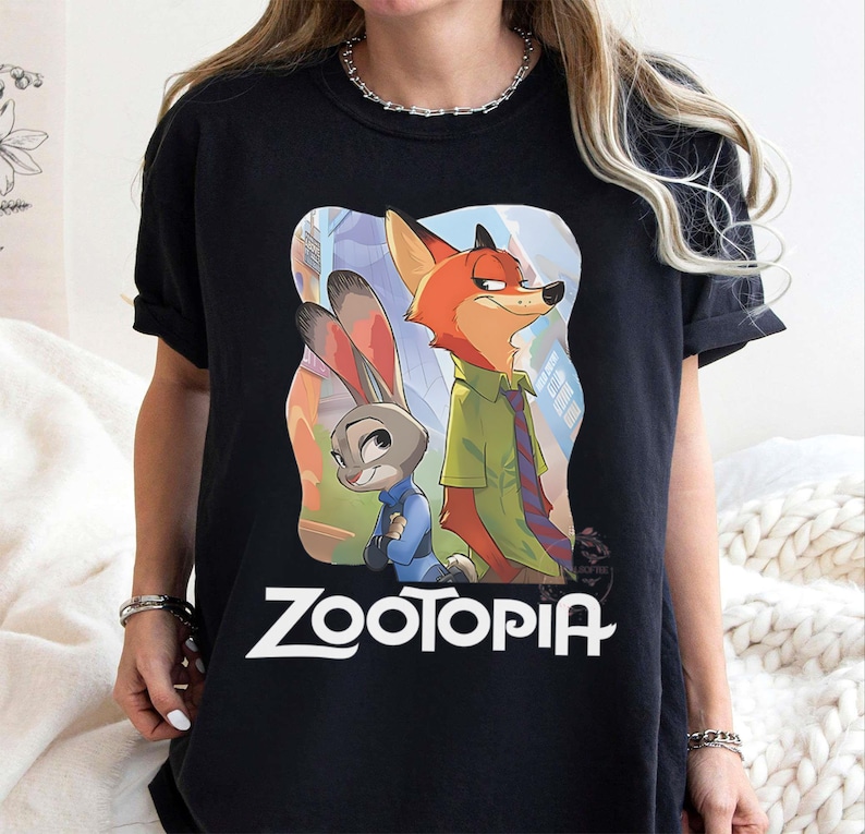 May include: Black t-shirt featuring the animated characters Judy Hopps and Nick Wilde from Zootopia. The graphic includes the movie title in white. The characters are set against a colorful background.