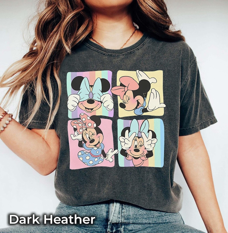 May include: A dark heather grey t-shirt with a graphic of four different images of Minnie Mouse. Each image shows Minnie Mouse with a different expression and pose. The background of the graphic is a rainbow of colors.